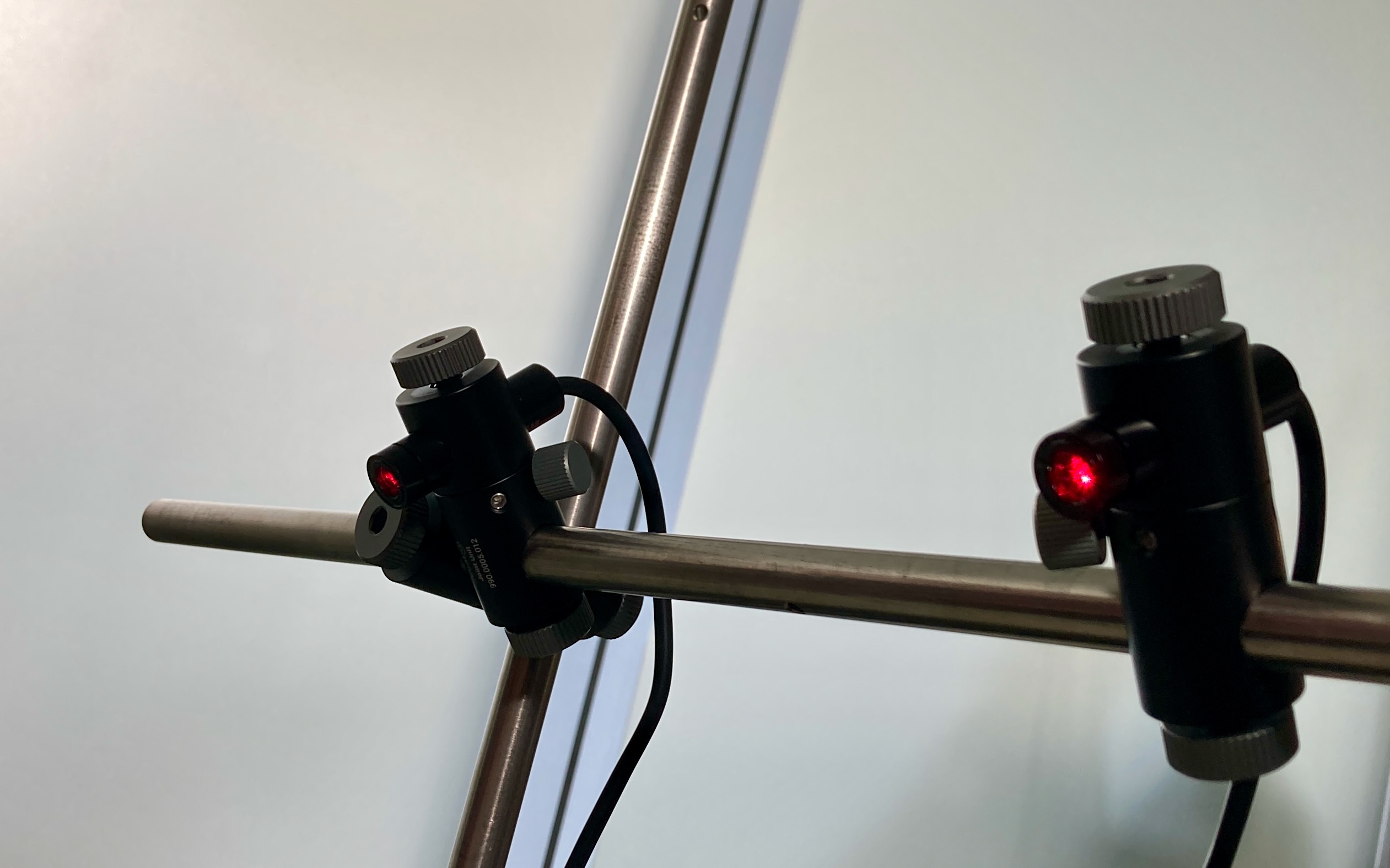 Zwei schwarze Laser-Module mit rot leuchtender Linse und Rändelschrauben an einer Metallstange: modularer Secabo Doppel-Kreuzlaser zum Positionieren