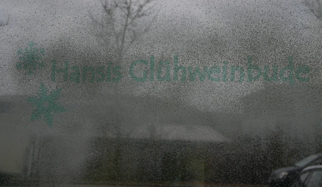 Mit Snow-Spray besprühte Fensterscheibe, darauf grüne Maskierfolie mit Schriftzug Hansis Glühweinbude und zwei Schneeflocken