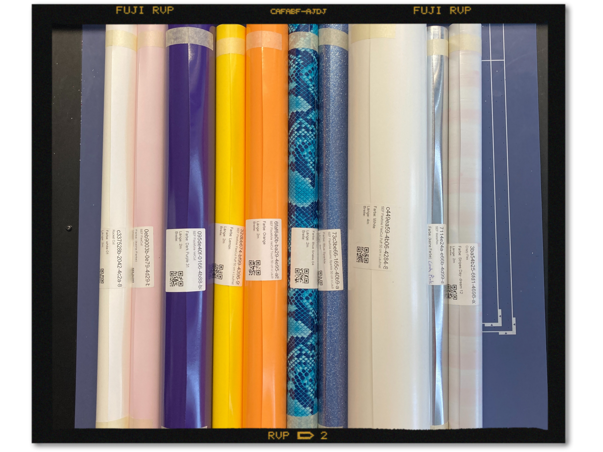 Aufgerollte SEF-Flexfolien nebeneinander, u. a. Weiß, Rosa, Dunkellila, Gelb, Orange, Blue Snake, Blue Sparkle und Metallic, mit Etiketten