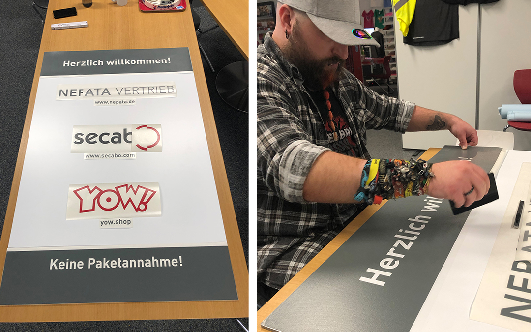 Links auf der Platte angeordnete Folienmotive von Nefata, Secabo und YOW, rechts drückt ein Mann den Schriftzug Herzlich willkommen mit Rakel an