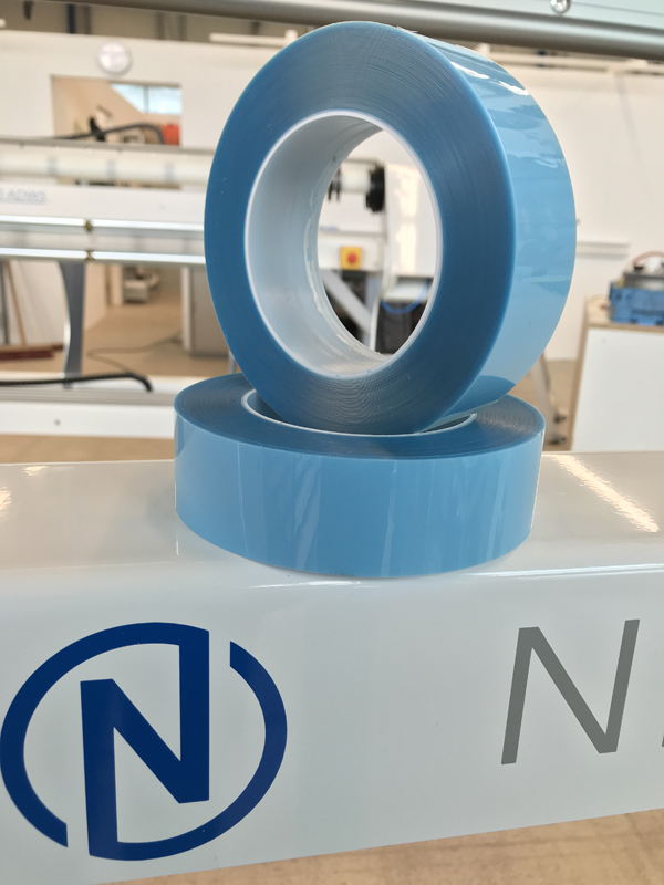 Zwei abgestochene Rollen blaue Steinschlagschutzfolie auf einer weißen Converting-Maschine mit blauem N-Logo in der Werkshalle