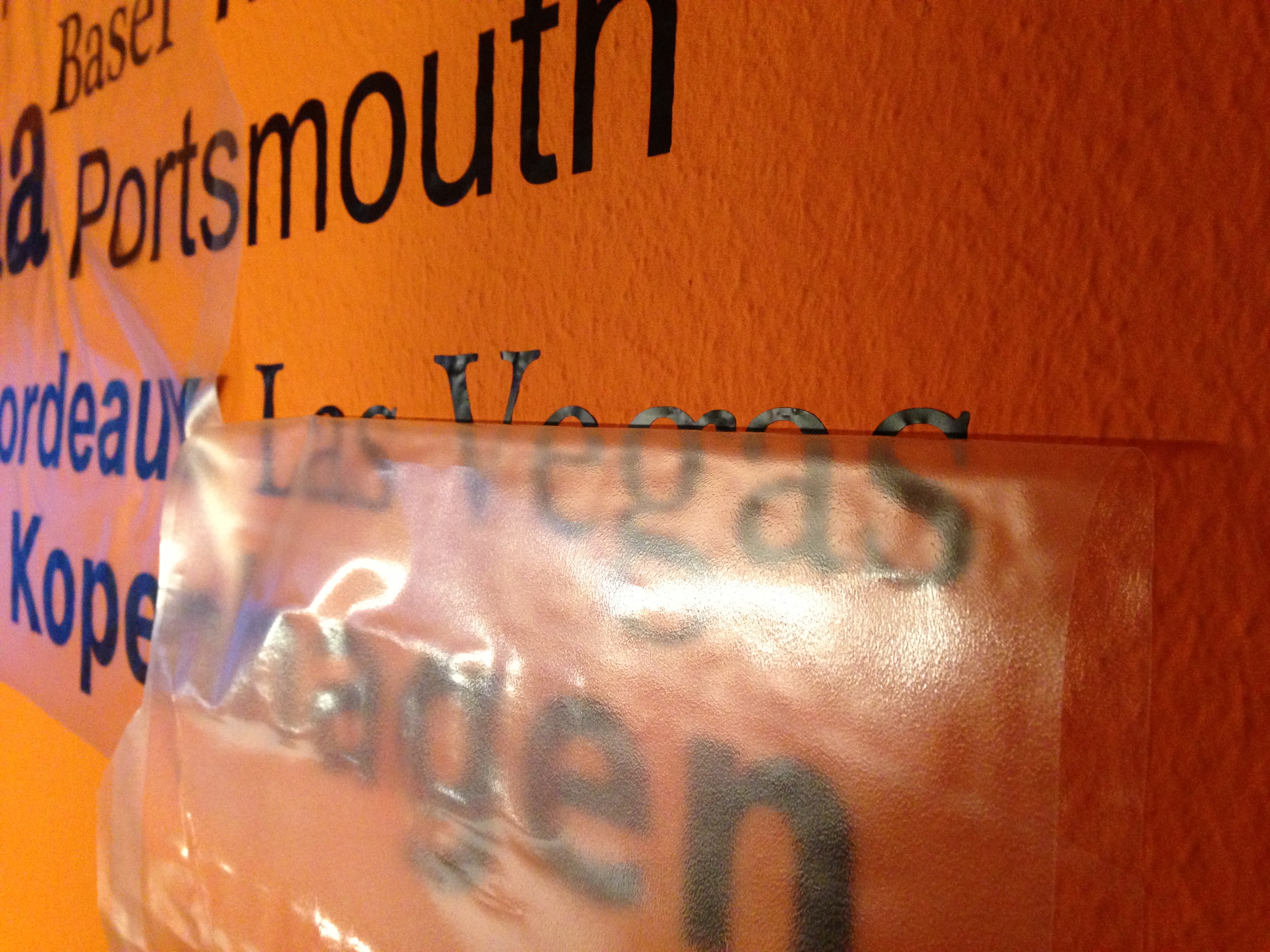 Transparentes Application Tape wird vom Wandtattoo mit Städtenamen wie Portsmouth und Las Vegas auf oranger Wand abgezogen