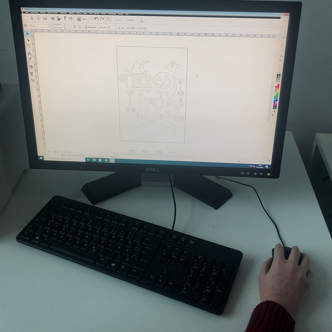 Monitor mit Plottersoftware: Trick-or-Treat-Motiv mit Kürbis, Geist, Hexenhut und Fledermaus als Schneidekonturen, Hand an der Maus