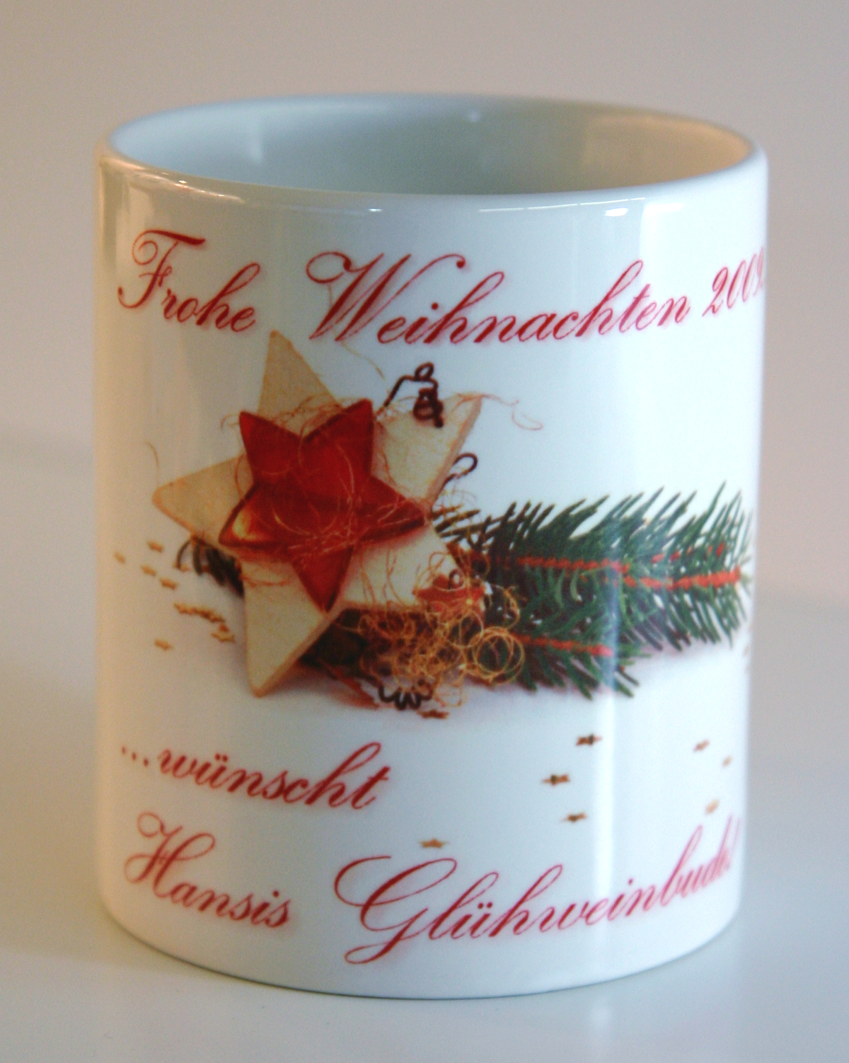 Fertig sublimierte weiße Tasse mit Stern, Tannenzweig und rotem Schriftzug Frohe Weihnachten 2009 … wünscht Hansis Glühweinbude