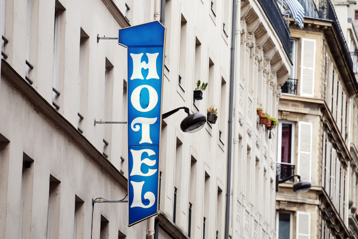 Senkrechtes blaues Hotelschild mit weißer Schrift an einer Altbaufassade, typisches Beispiel für Leuchtreklame mit transluzenter Folie