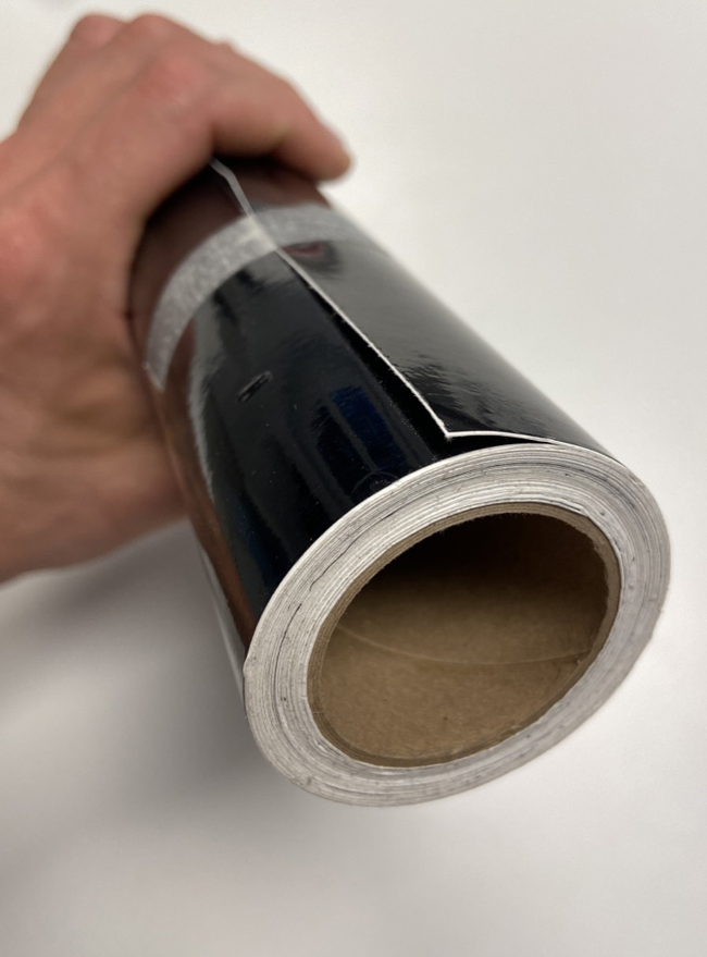 Hand hält kleine, kompakte Rolle schwarzer Glanzfolie auf Papphülse mit 40mm Innendurchmesser, Blick auf die Hülsenöffnung