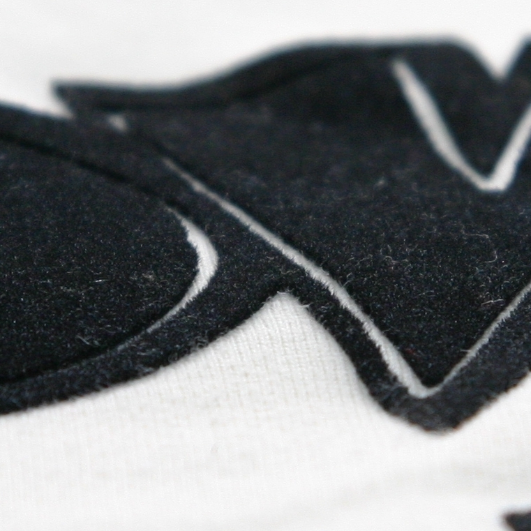Nahaufnahme schwarzer Flockfolie auf weißem Textil, samtig-faserige Oberfläche mit geplotteten Buchstabenkonturen und feinen Aussparungen