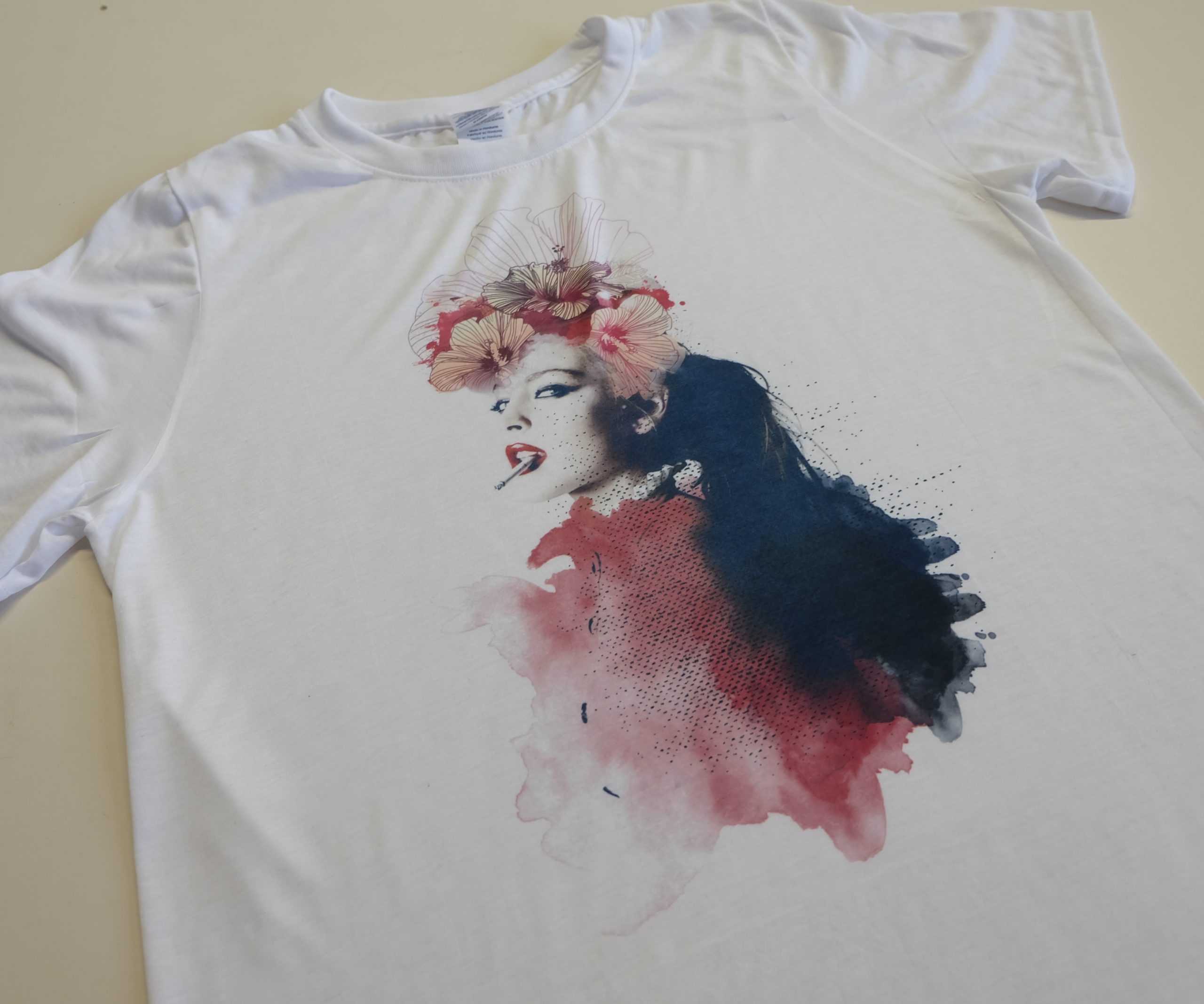 Weißes T-Shirt mit Sublimationsdruck: Frauenporträt mit Hibiskusblüten im Haar und Zigarette, umgeben von roten und blauen Aquarellflecken