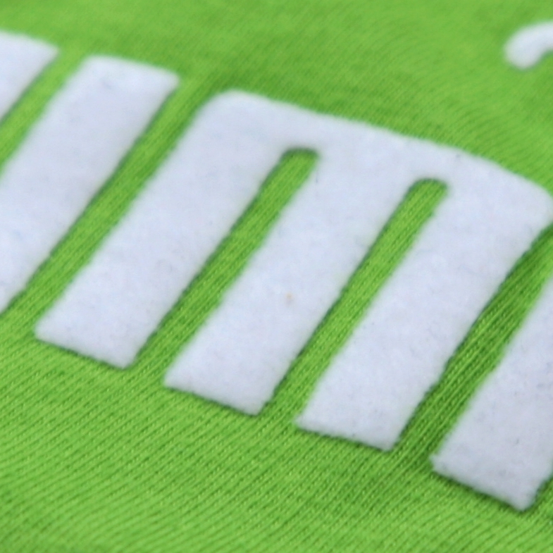 Nahaufnahme weißer Buchstaben aus Flockfolie auf grünem Shirtstoff, die samtig-matte Oberfläche der aufgepressten Folie ist gut erkennbar