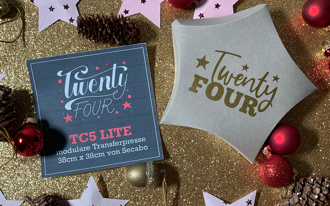 Sternförmige Adventskalenderbox mit goldenem Twenty-Four-Schriftzug, Karte zur Secabo TC5 Lite, rosa Papiersterne und rote Kugeln auf Goldglitter