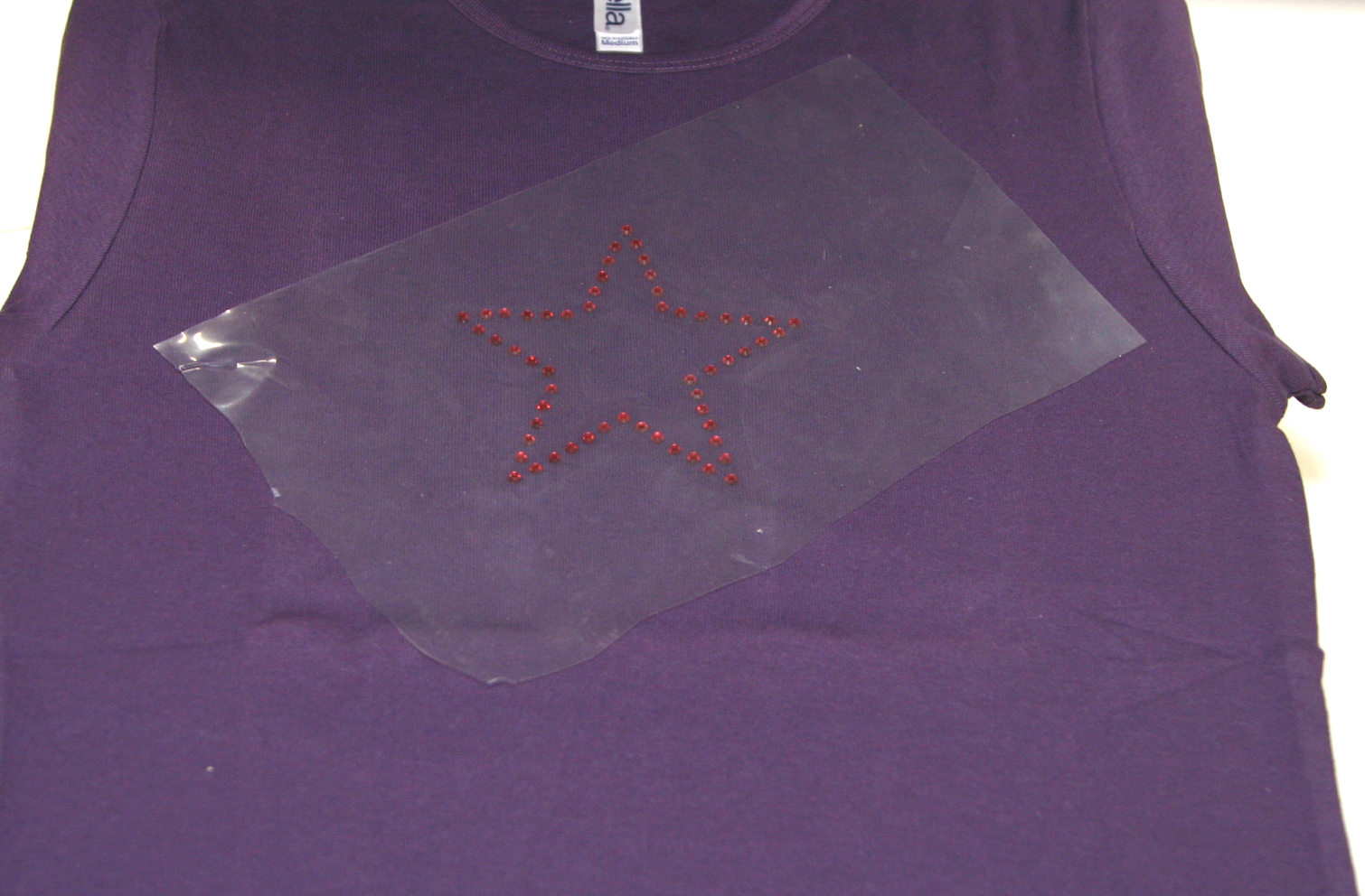 Sternmotiv aus roten Strass-Steinen unter transparenter Übertragungsfolie auf einem lila Shirt, bereit zum Aufpressen