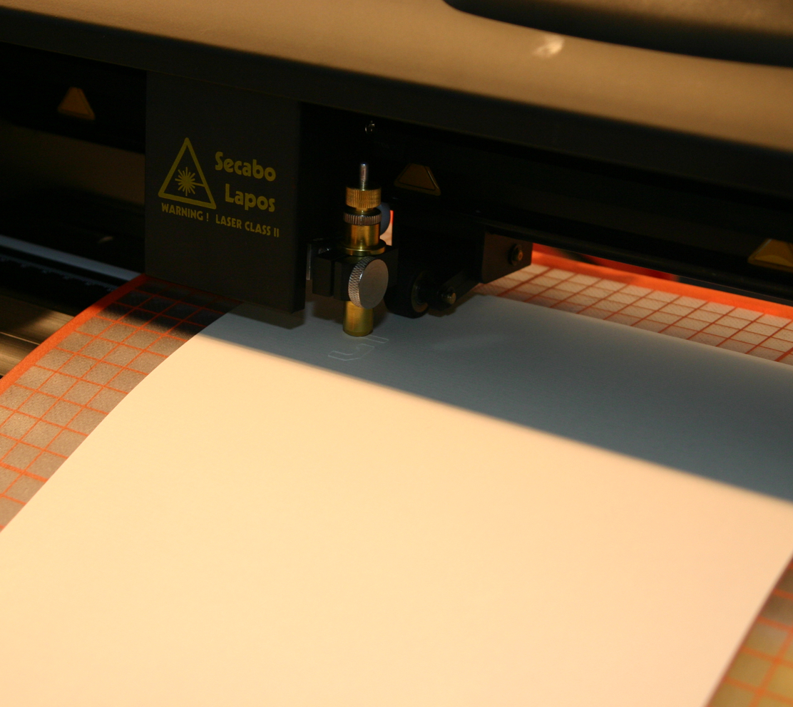 Schneideplotter Secabo Lapos schneidet Buchstaben in weißen Karton auf orange gerasterter Plotunterlage – Schritt beim Basteln der Weihnachtskarten