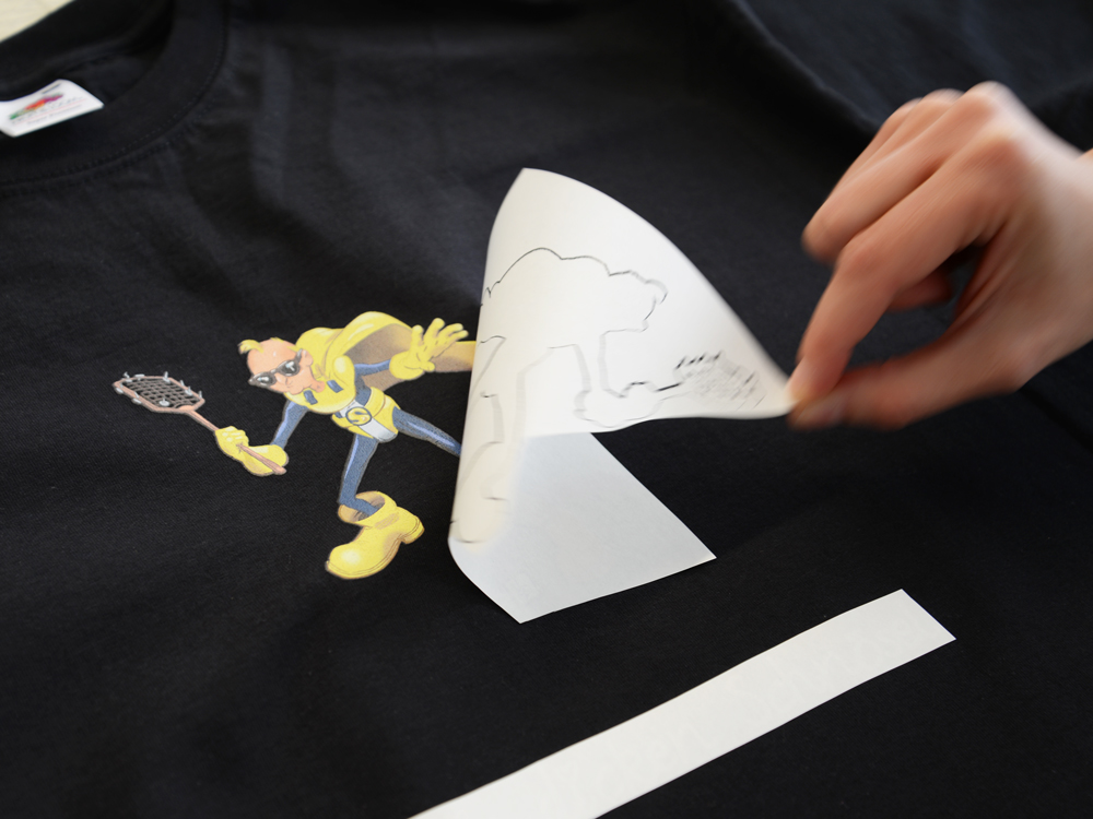Hand zieht Trägerschicht von schwarzem Shirt ab, darunter die aufgepresste gelbe Comic-Superheldenfigur mit Fliegenklatsche