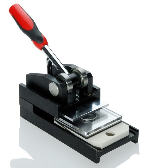 Schwarze Multifunktionsstanzpresse mit rot-schwarzem Hebelgriff und Acrylplatten zum passgenauen Ausstanzen von Papiermotiven für Buttons