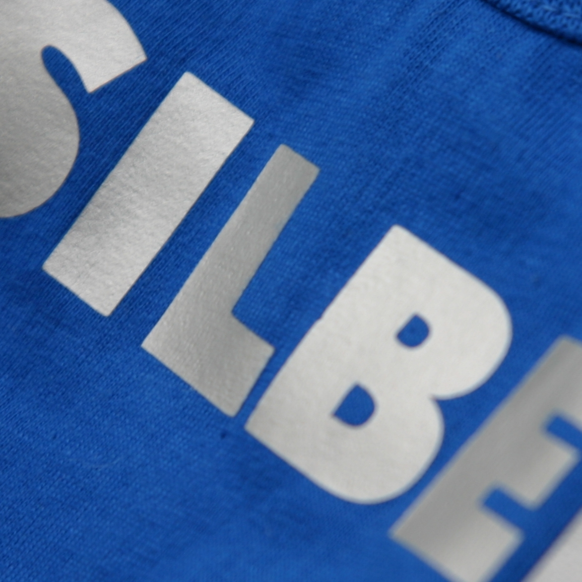 Nahaufnahme eines blauen Textils mit dem Schriftzug SILBER aus aufgepresster, glänzend silberner Flexfolie
