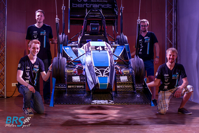 Vier Teammitglieder von BRS Motorsport posieren am Rennwagen E45 mit blau-weißer Folierung und Sponsorenaufklebern