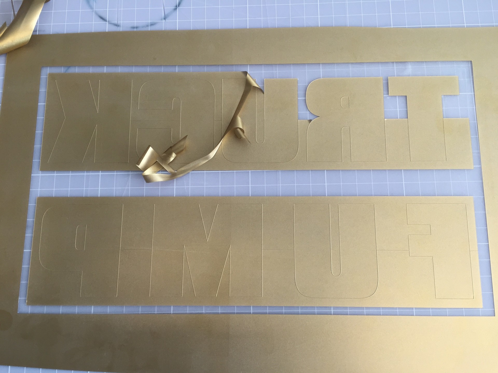 Goldene Flexfolie mit gespiegeltem Schriftzug TRUCK FUMP beim Entgittern, überschüssige Folie wird um die Buchstaben abgezogen