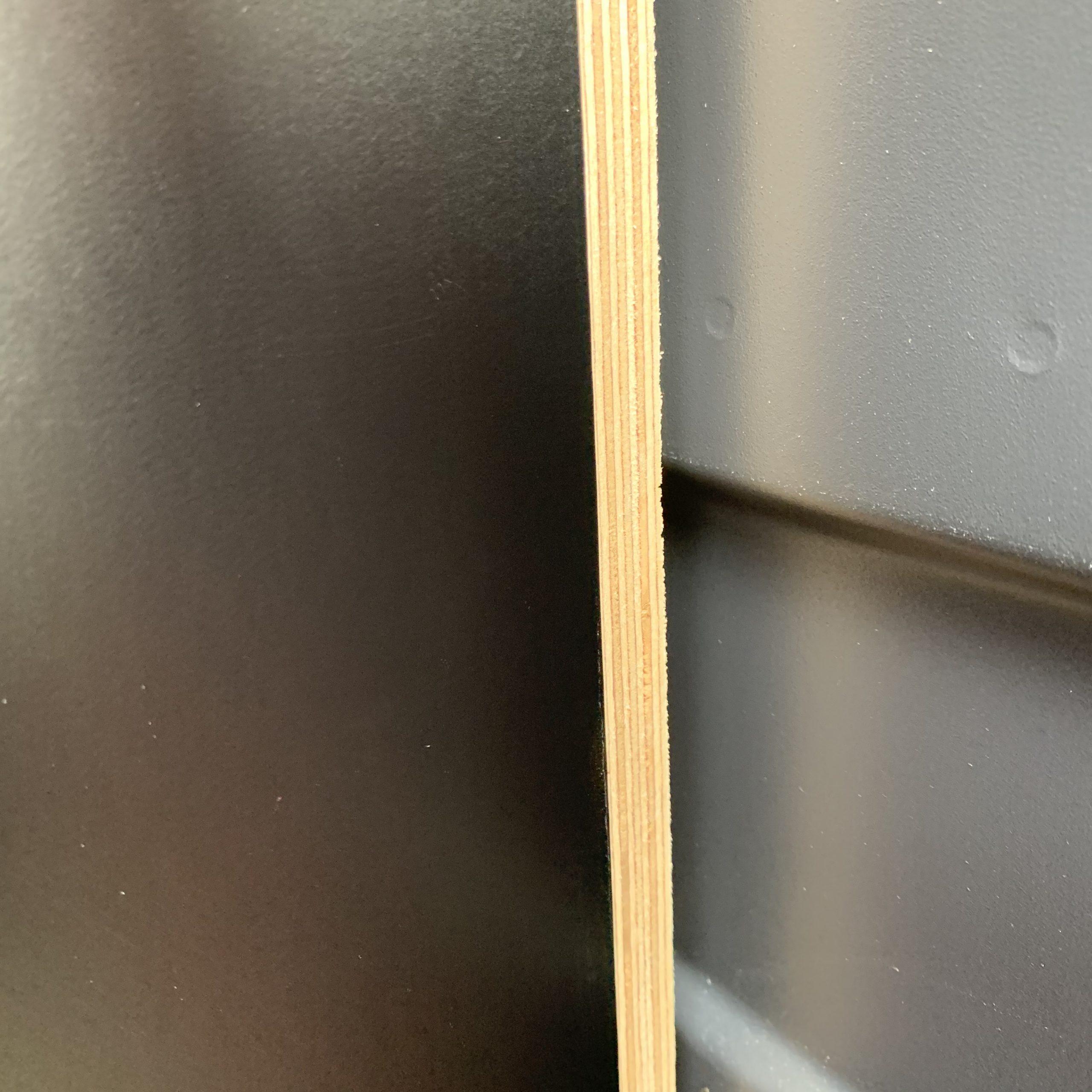 Nahaufnahme einer Sperrholzplatte mit schwarzer, matter Selbstklebefolie, die bündig an der hellen Holzkante abgeschnitten ist