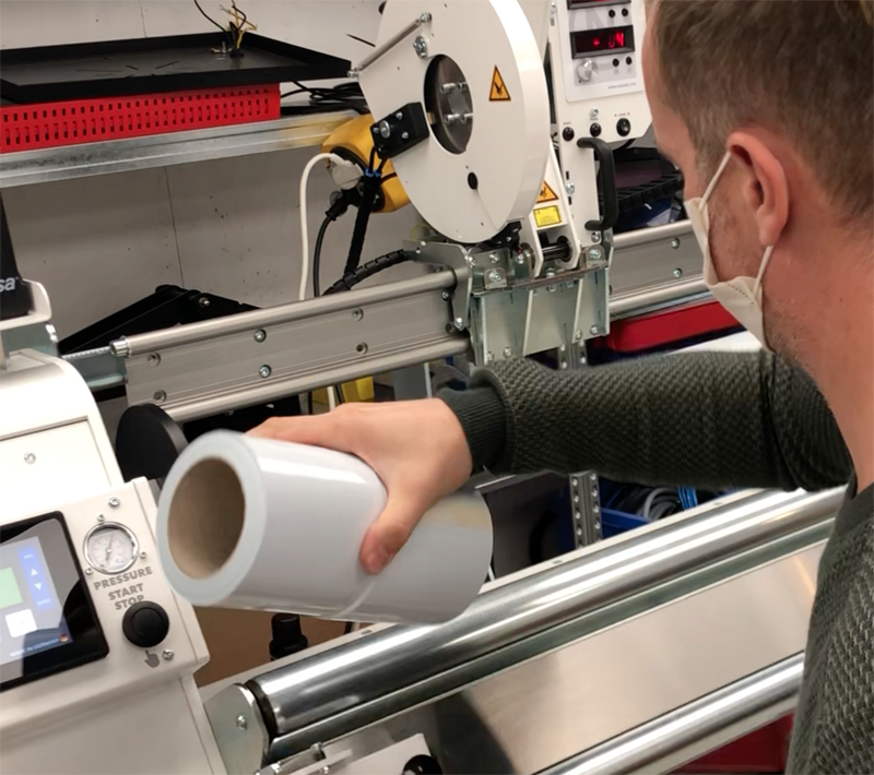 Mitarbeiter hält sauber abgestochene Rolle weißer Ritrama Klebefolie vor der NEPATA 1900 ADWS Abstechmaschine