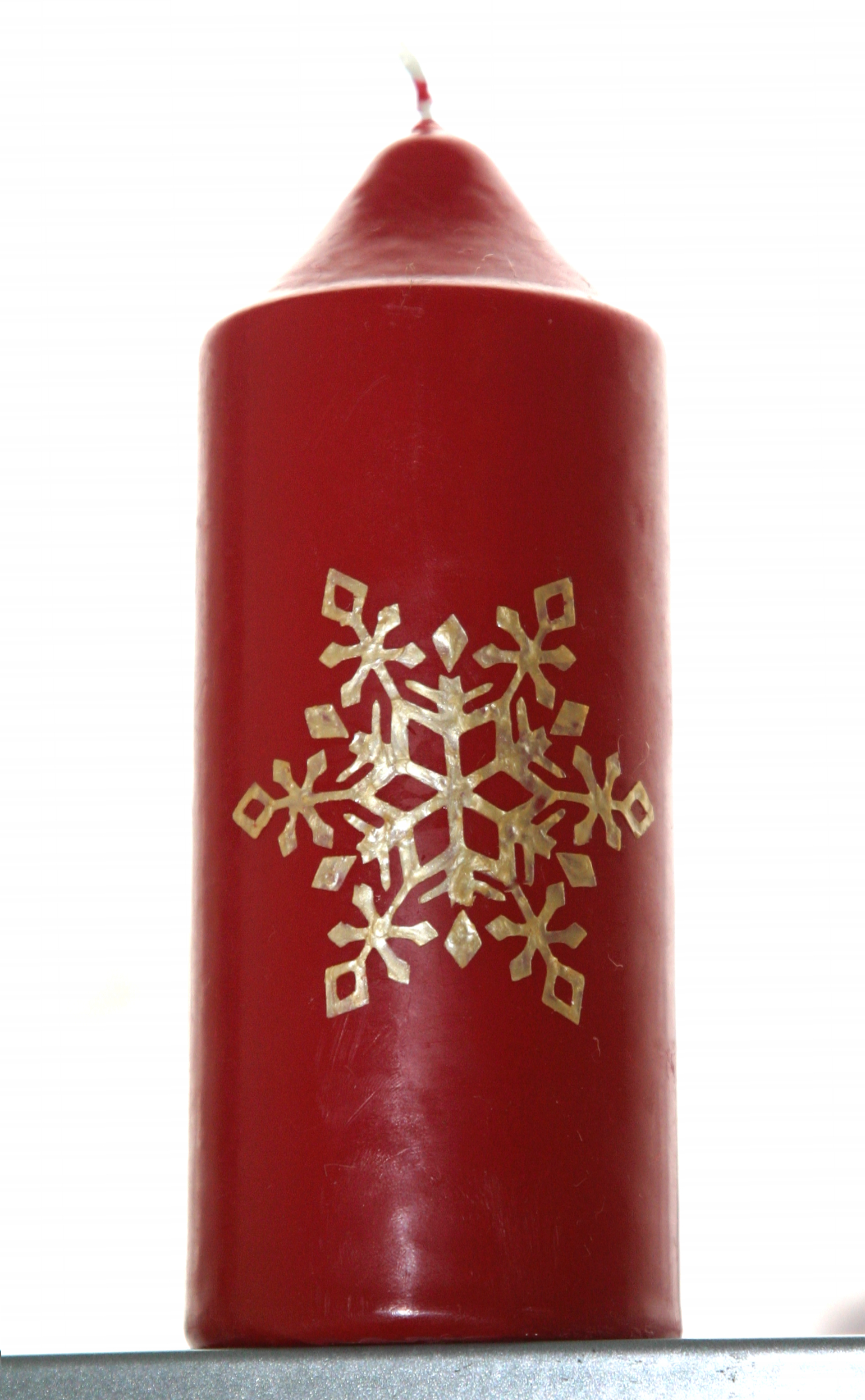 Rote Stumpenkerze mit selbst aufgebrachtem goldenem Schneekristall-Motiv aus Wachs, seitlich liegend fotografiert auf silbernem Untergrund