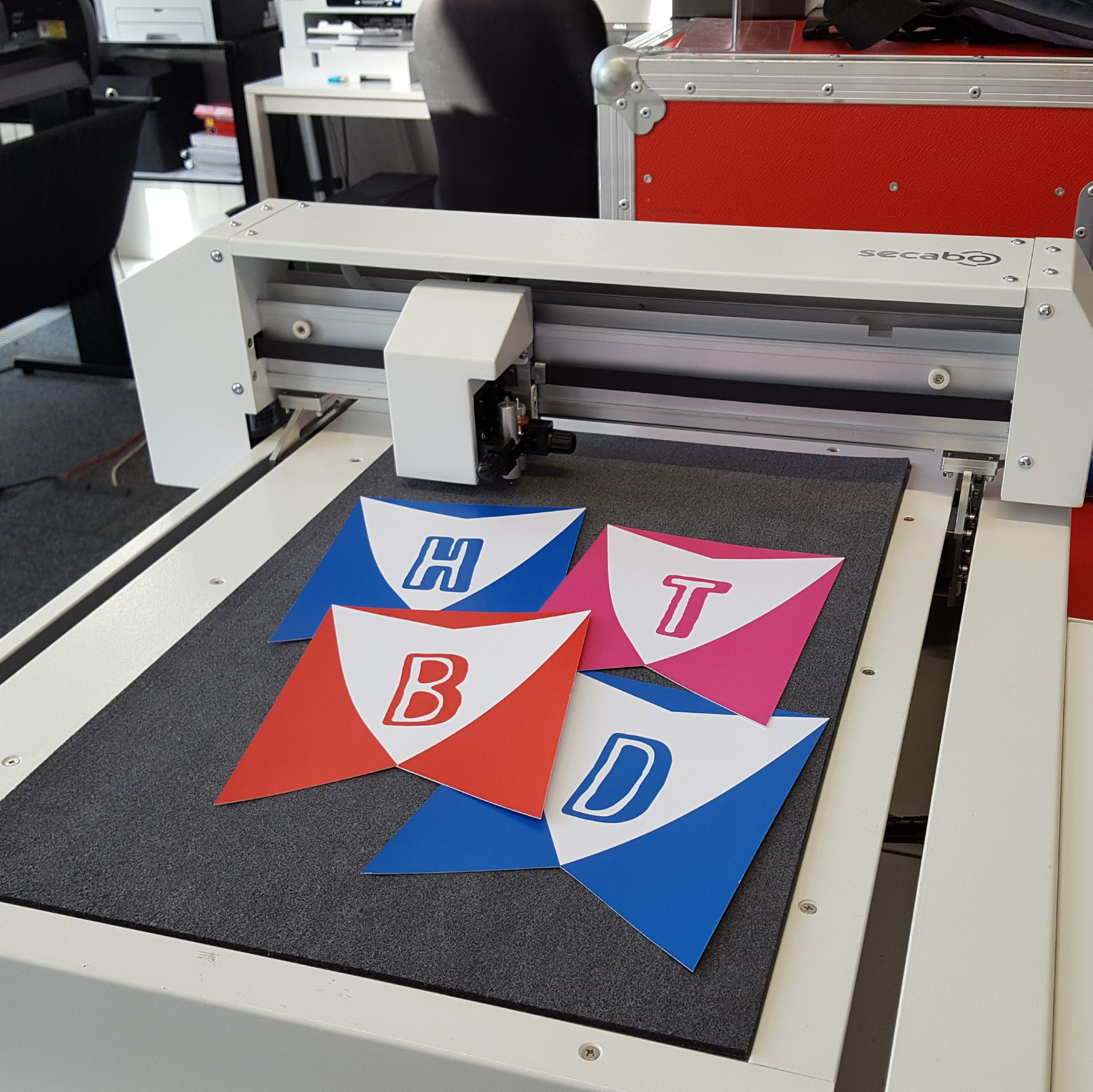 Flachbett-Schneideplotter von Secabo mit selbst geschnittenen Wimpeln in Blau, Rot und Pink mit den Buchstaben H, T, B und D für eine Girlande
