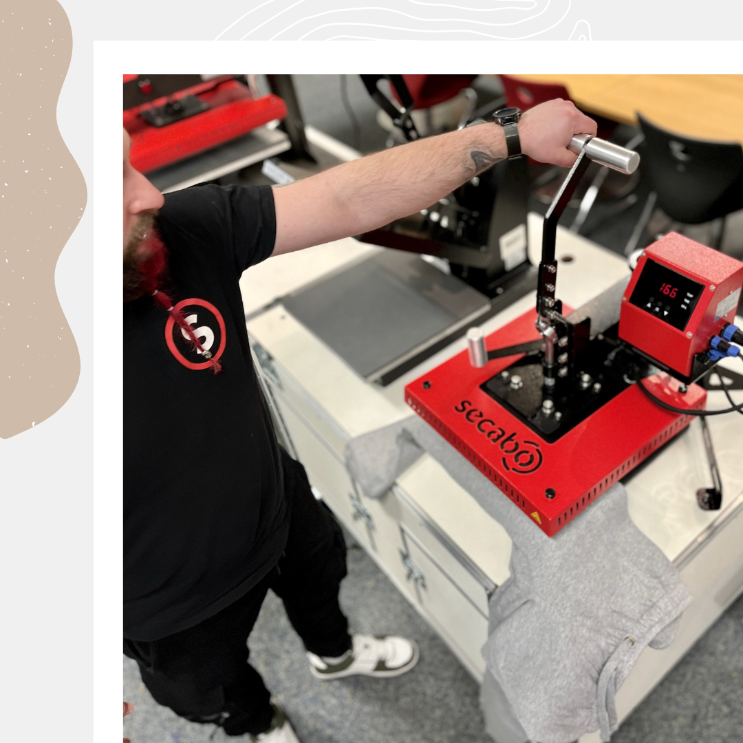Mann schließt die rote Secabo TS5 Economy Swingpresse per Hebel, graues Textil liegt auf der Unterplatte, Display zeigt 156