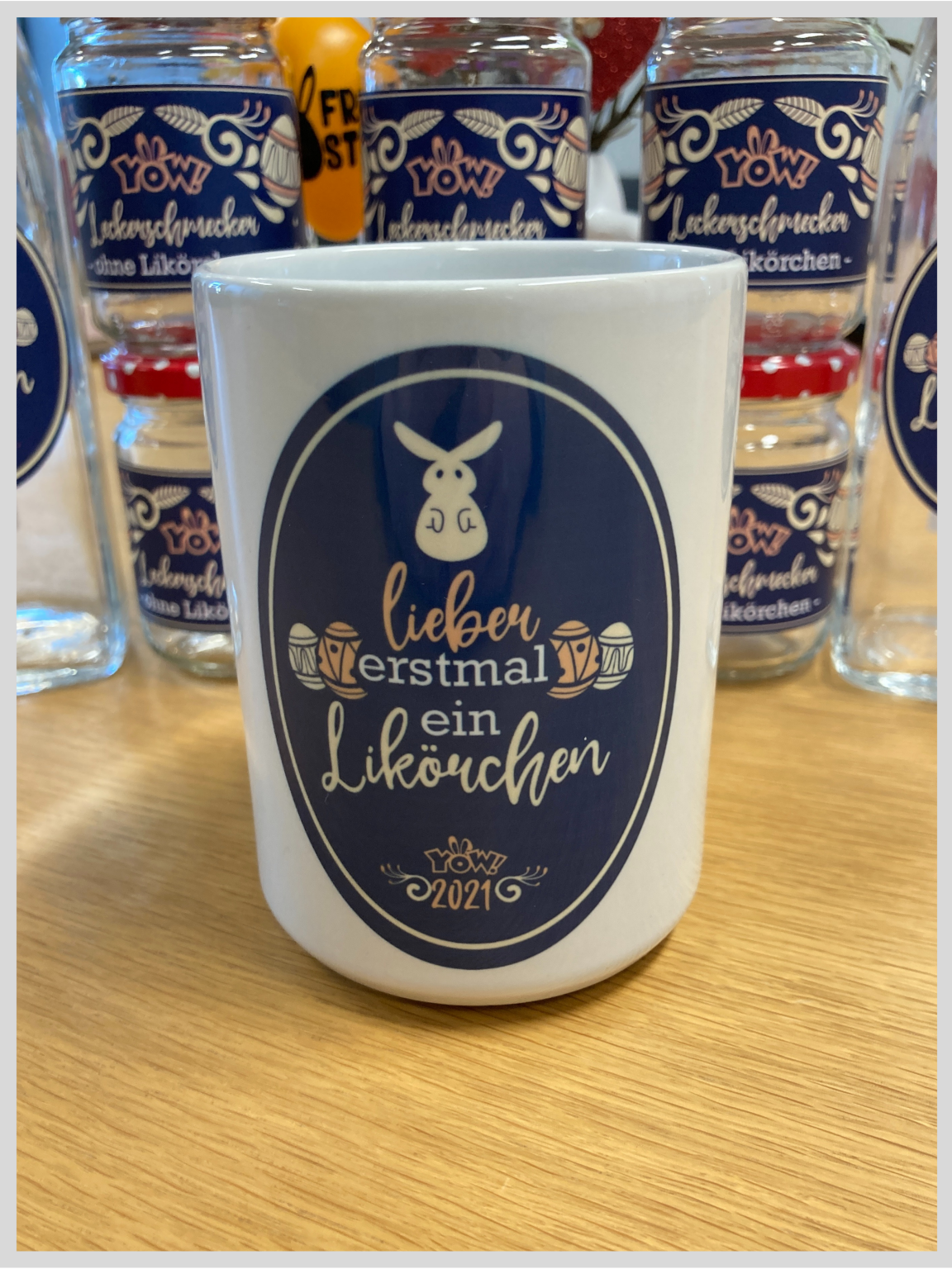 Sublimierte weiße Tasse mit Hasen, Ostereiern und Aufschrift lieber erstmal ein Likörchen, YOW! 2021, dahinter Gläser mit passenden Etiketten