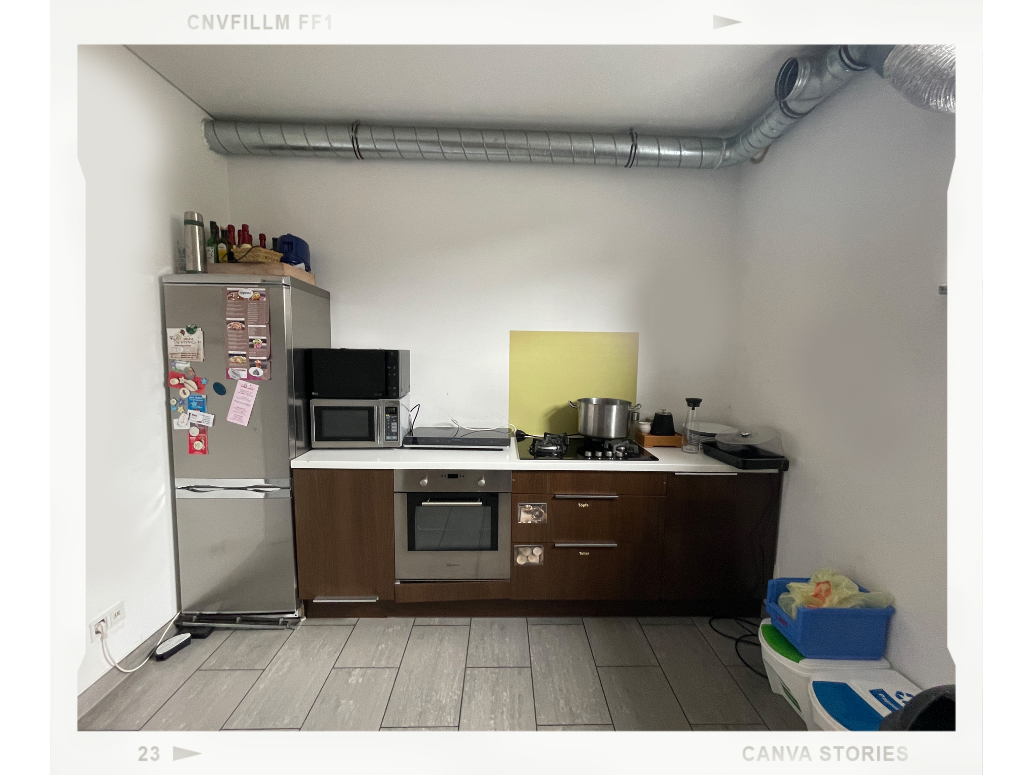 Firmenküche vorher: dunkelbraune Unterschränke, Edelstahl-Kühlschrank, gestapelte Mikrowellen, gelbe Spritzschutzplatte, kahle weiße Wände
