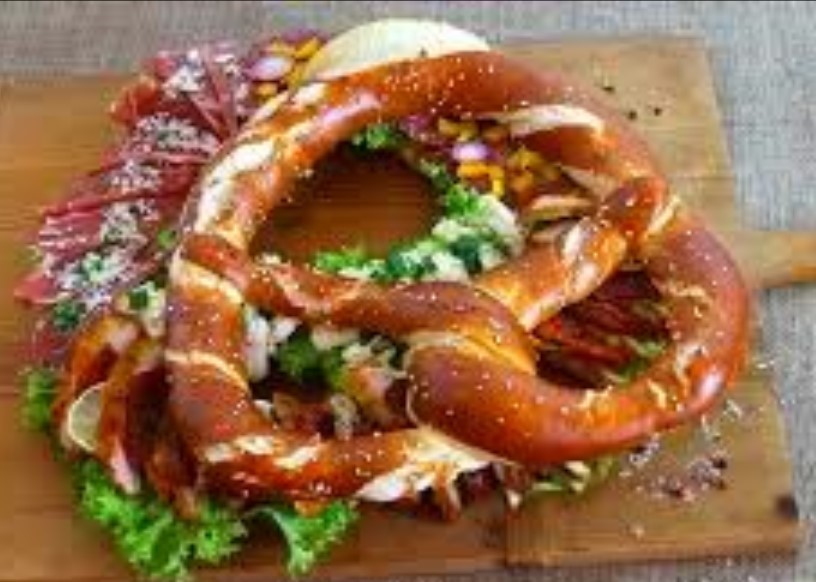 Große gefüllte Brezel mit Salami, Salat und Zwiebeln auf einem Holzbrett, Brotzeit für die Teilnehmer des YOW! Kreativ-Workshops