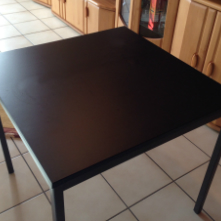 Quadratischer Tisch mit mattschwarzer Tischplatte nach dem Bekleben mit Selbstklebefolie, in einer Küche mit Fliesenboden und Holzschränken