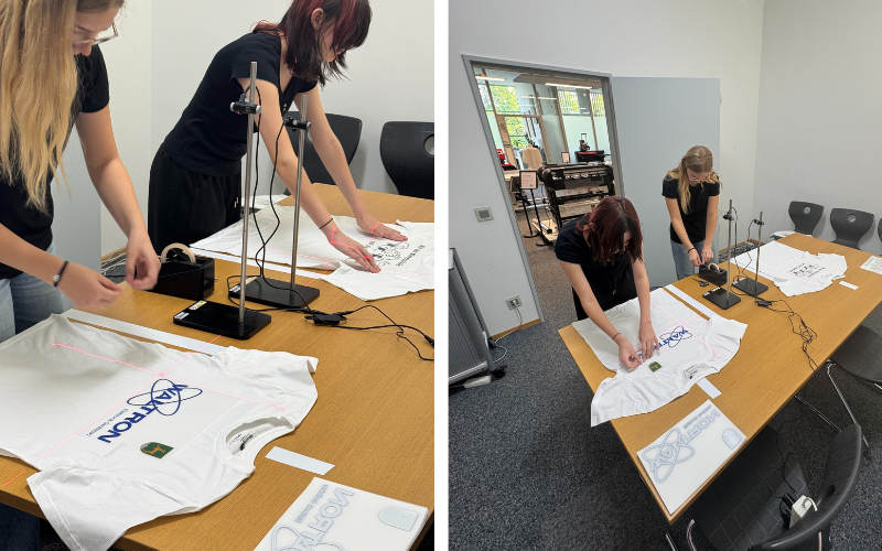 Schülerinnen richten Transfers auf weißen T-Shirts mit Secabo Kreuzlasern auf Stativen aus, rote Laserlinie auf dem Shirt sichtbar