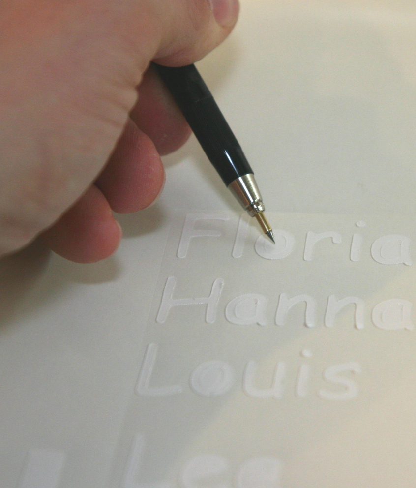 Hand entgittert mit einem Entgitterstift die geplotteten Namen Florian, Hanna und Louis auf weißer Schneidefolie für Christbaumkugeln