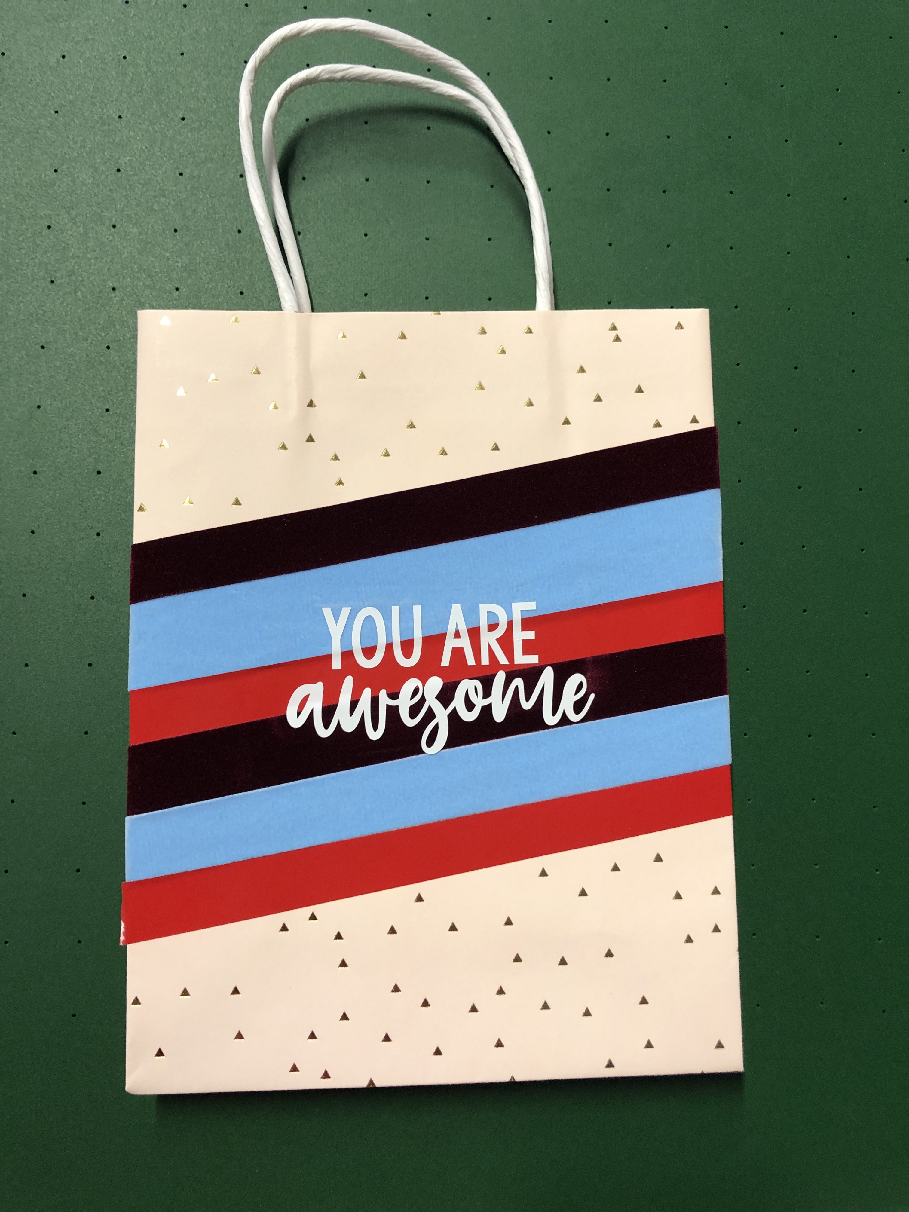 Rosa Geschenktüte mit Goldmuster, beklebt mit diagonalen Folienstreifen in Bordeaux, Hellblau und Rot und weißem Schriftzug You are awesome
