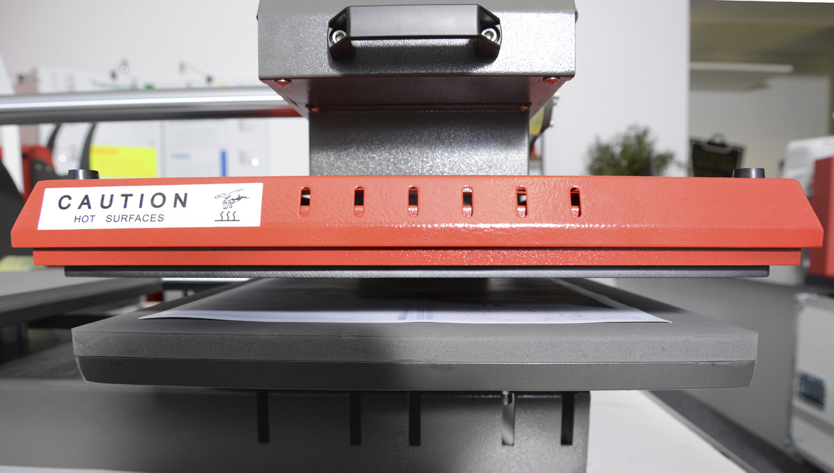 Leicht geöffnete Transferpresse mit roter Heizplatte, darunter trocknet das bedruckte Sublimationspapier 30–45 Sekunden lang