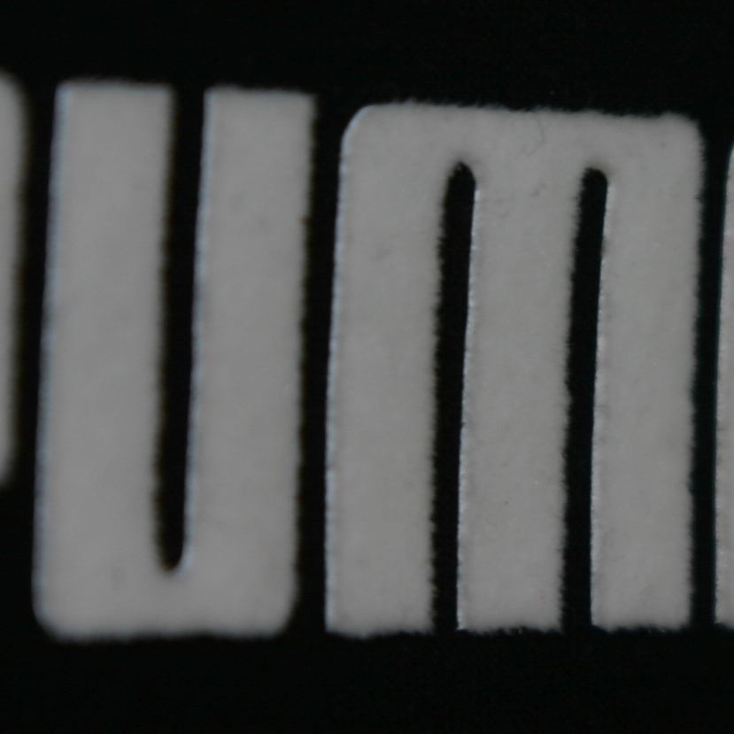 Nahaufnahme eines weißen Puma-Schriftzugs aus Flockfolie auf schwarzem Textil, die samtige Oberfläche und die Schnittkanten sind gut erkennbar