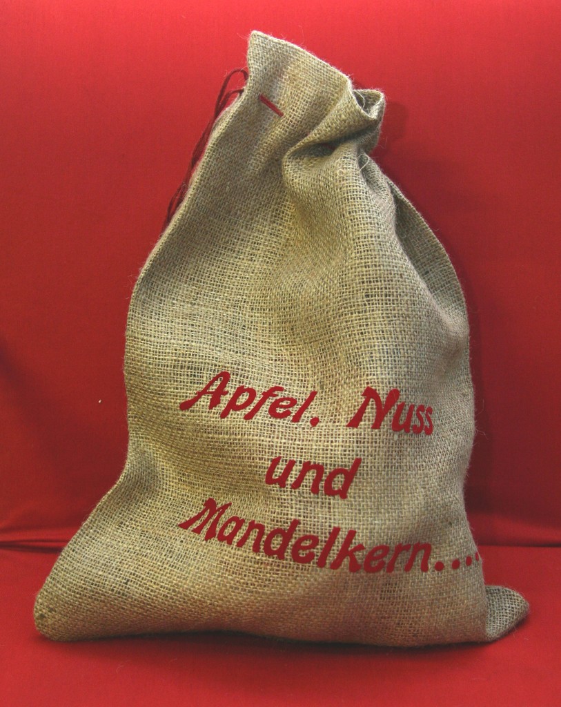 Nikolaussäckchen aus Jute mit aufgebrachter roter Flockfolien-Schrift Apfel, Nuss und Mandelkern vor rotem Hintergrund