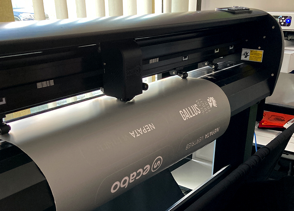 Schneideplotter mit eingelegter grauer Folie, in die Logos und Schriftzüge geschnitten werden, als Vorbereitung fürs Sandstrahlen