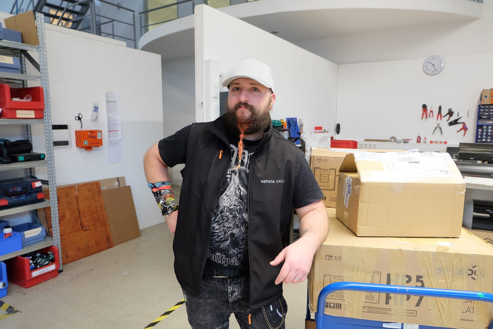 Application engineer Edwin (Ääd), wearing a Nepata Group vest, is leaning against some parcels on a trolley in the workshop, which features a tool rack