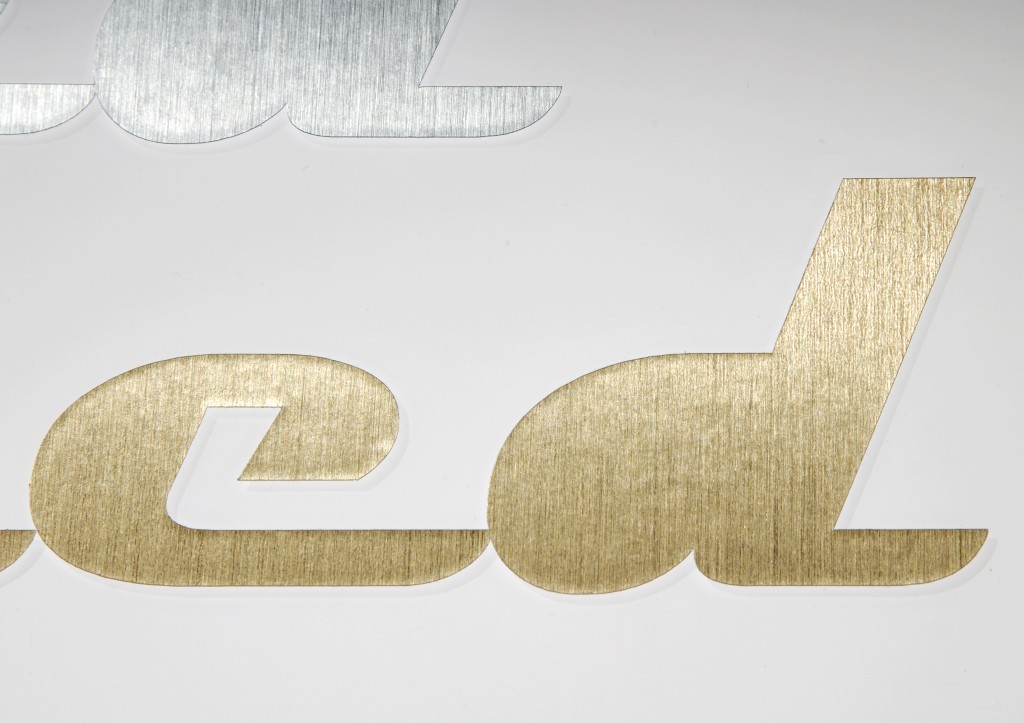 Geplottete Buchstaben aus Klebefolie mit gebürstetem Metalleffekt in Gold und Silber auf weißem Untergrund