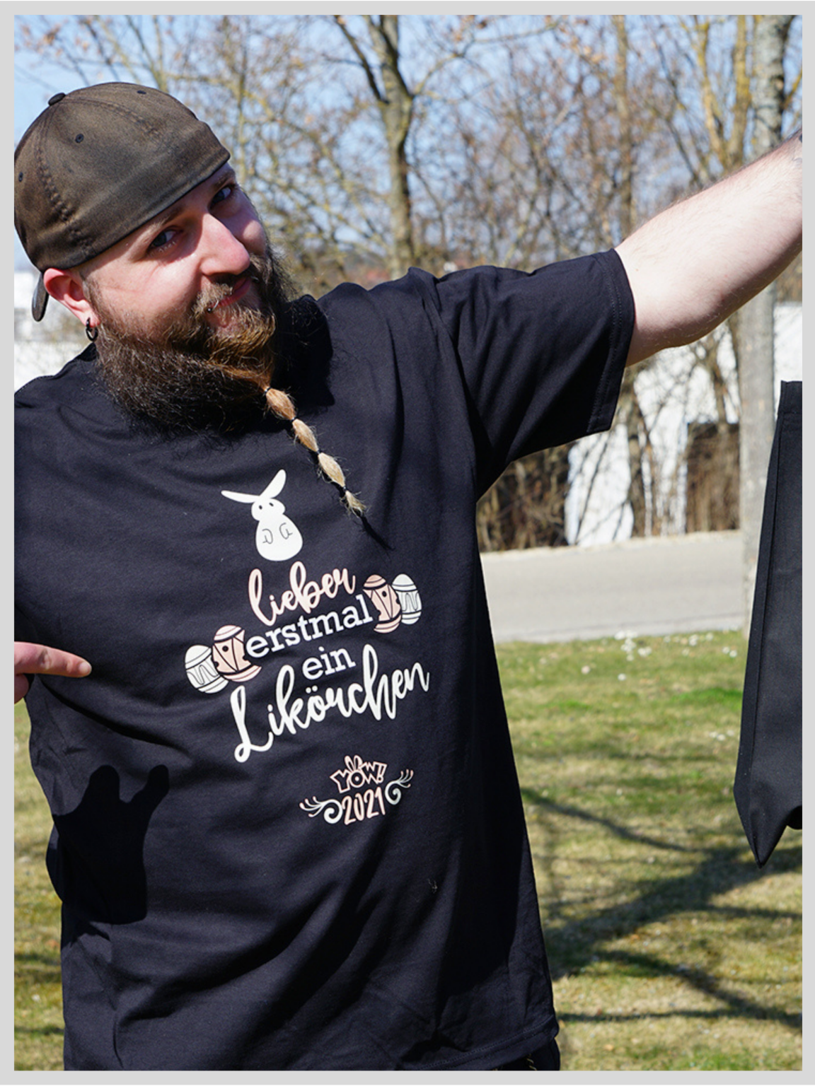 Mann in schwarzem Shirt mit Flexfolien-Osterdruck: Hase, Ostereier und Spruch lieber erstmal ein Likörchen, YOW! 2021; daneben schwarze Stofftasche