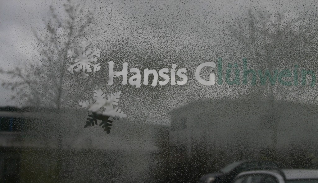 Fensterscheibe mit Snow-Spray: Schriftzug Hansis Glühwein und Schneeflocken, Maskierfolie teils abgezogen, teils noch aufgeklebt