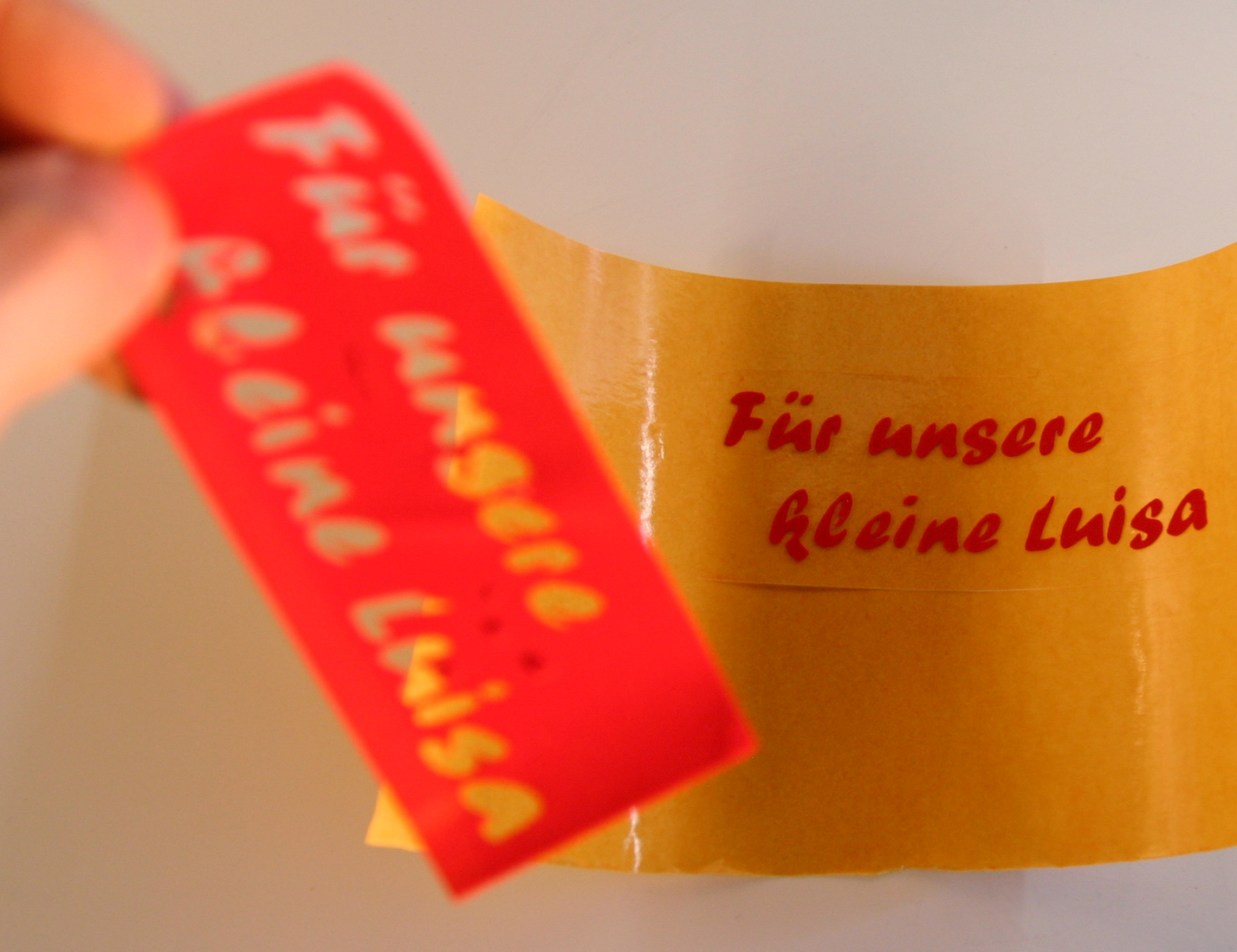 Entgitterter roter Flockfolien-Schriftzug Für unsere kleine Luisa auf Übertragungsfolie, daneben das abgezogene Restgitter in der Hand