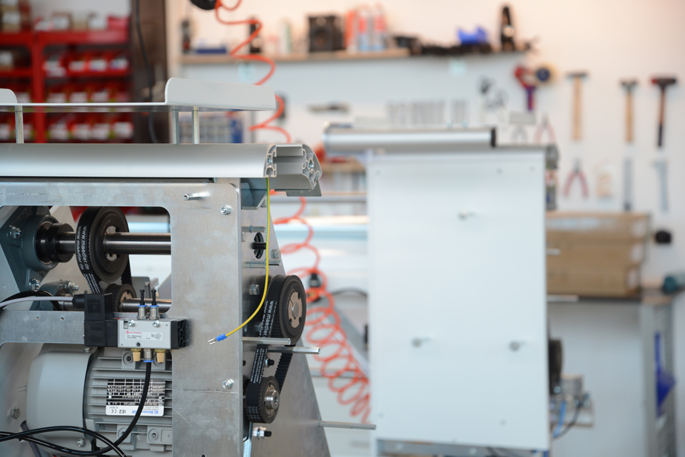 Machine ouverte équipée d'une transmission par courroie crantée, d'une vanne pneumatique et d'un moteur électrique dans l'atelier d'entretien ; à l'arrière-plan, des outils et un tuyau d'air comprimé
