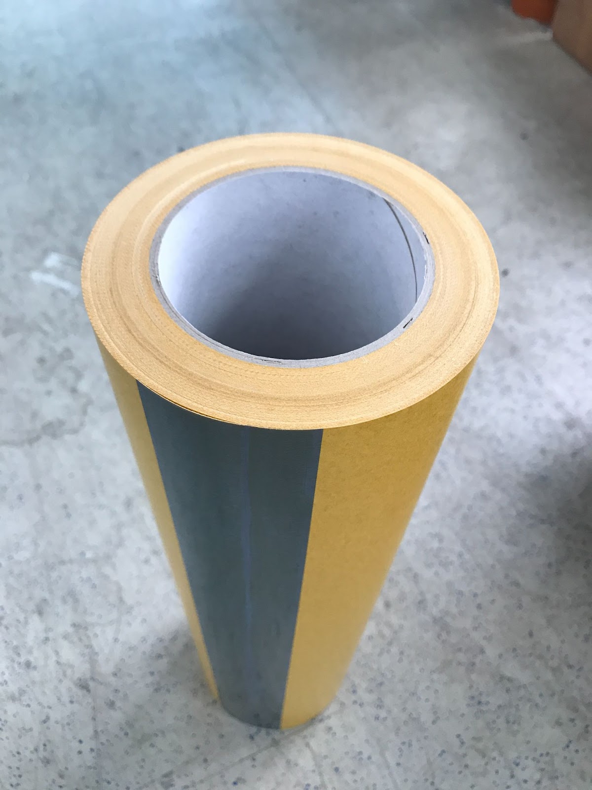 Stehende Mutterrolle doppelseitiger Klebefolie mit gelbem Glassine-Liner und Kartonkern auf Betonboden, Ausgangsmaterial für den Abstechtest