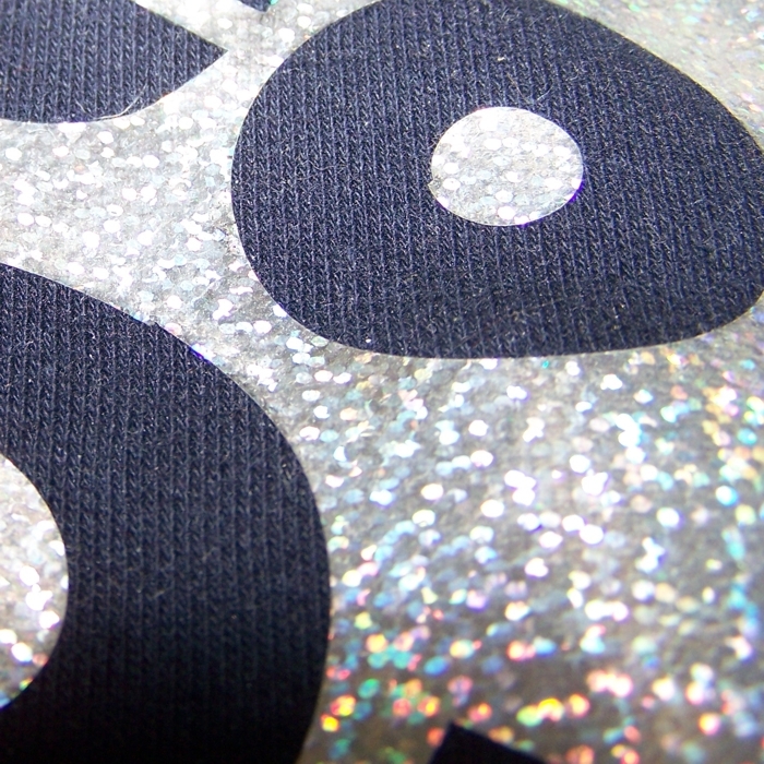 Nahaufnahme: silberne Glitzer-Flexfolie mit Hologrammeffekt auf dunkelblauem Strickstoff, ausgeplottete runde Formen zeigen den Stoff
