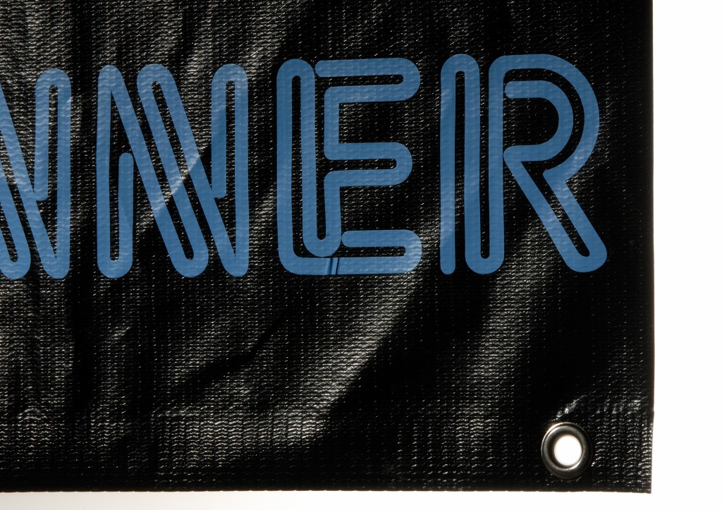 Schwarzes Werbebanner mit blauem Folienschriftzug NNER und Metallöse in der Ecke, beklebt mit Ritrama banner Folie