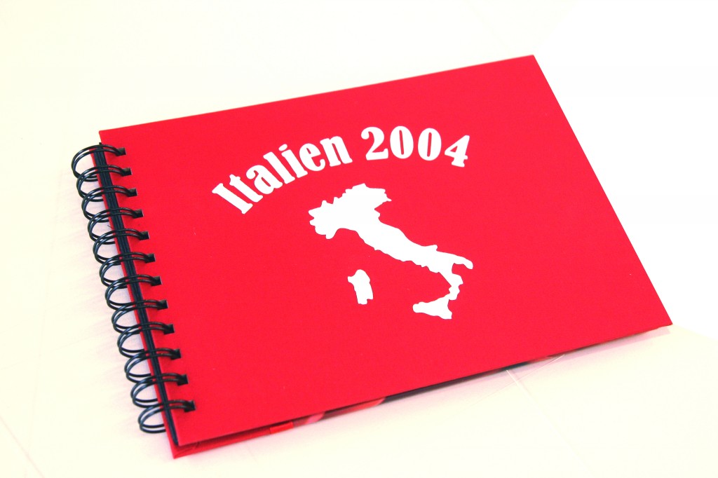 Rotes Spiralbuch, mit weißer Flockfolie beschriftet: Schriftzug Italien 2004 über einer Silhouette der Landkarte Italiens