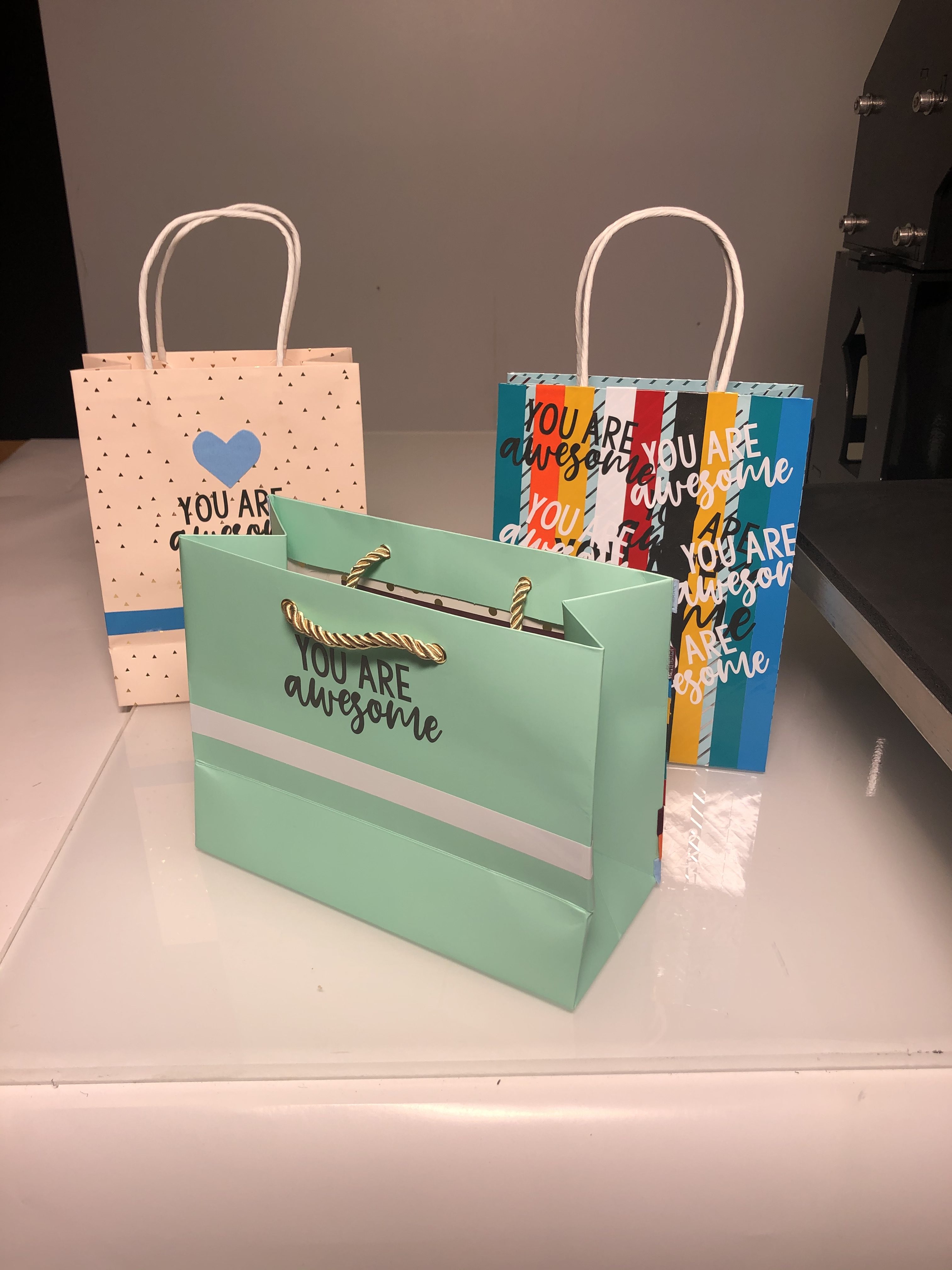 Drei mit Selbstklebefolie beklebte Geschenktüten: Schriftzug YOU ARE awesome, weiße und blaue Streifen, blaues Herz – fertiges Ergebnis