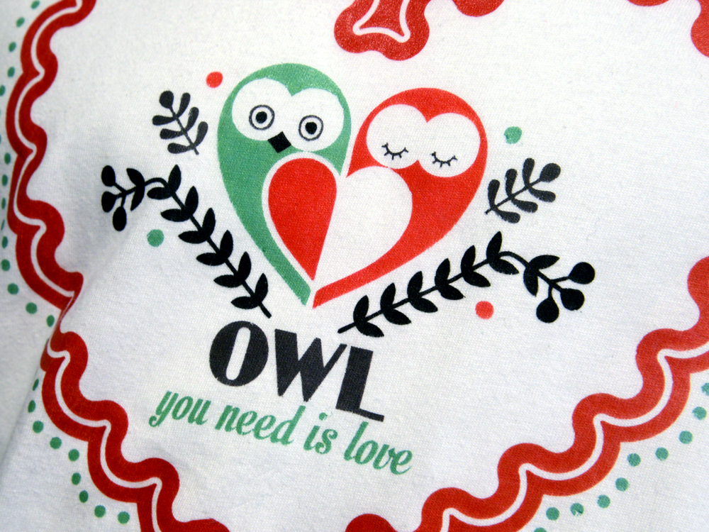 Mit Laser No Trim übertragene Grafik auf weißem Stoff: grüne und rote Eulen in Herzform, Schriftzug OWL you need is love, roter Wellenrahmen