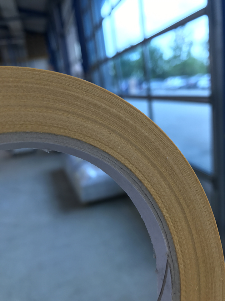 Primer plano del borde de corte de un rollo de cinta adhesiva doble cortado, con un revestimiento de papel glassine sobre un núcleo de cartón, cortado limpiamente